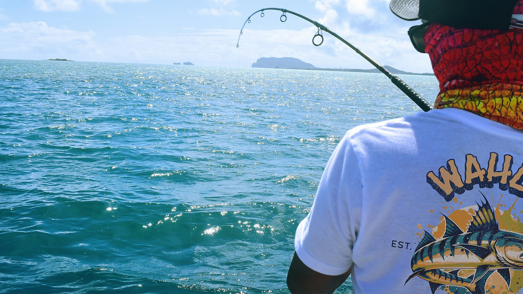 Person fishing in the ocean with a colorful fish design on their shirt.